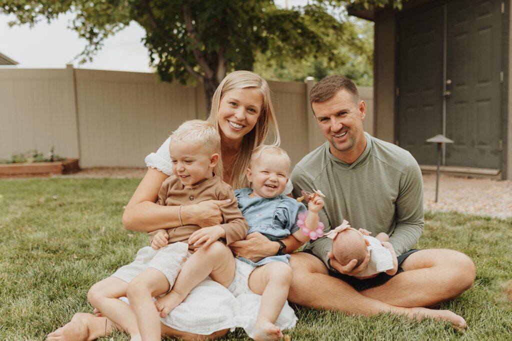 Casual outdoor photo of Dr. Ryan Helgerson and his family sitting together on a grassy lawn.