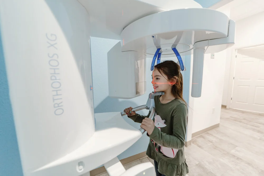 A young girl standing in a dental imaging machine (ORTHOPHOS XG) preparing for a panoramic dental X-ray.