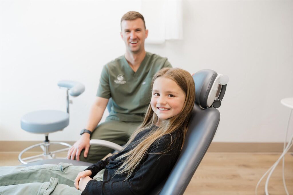 Dental professional at Bookcliff Family Dental in Grand Junction, CO, seated beside a young patient in a reclining chair, engaging in a consultation that underscores the clinic’s commitment to gentle, preventative care in a comfortable, child-friendly setting.
